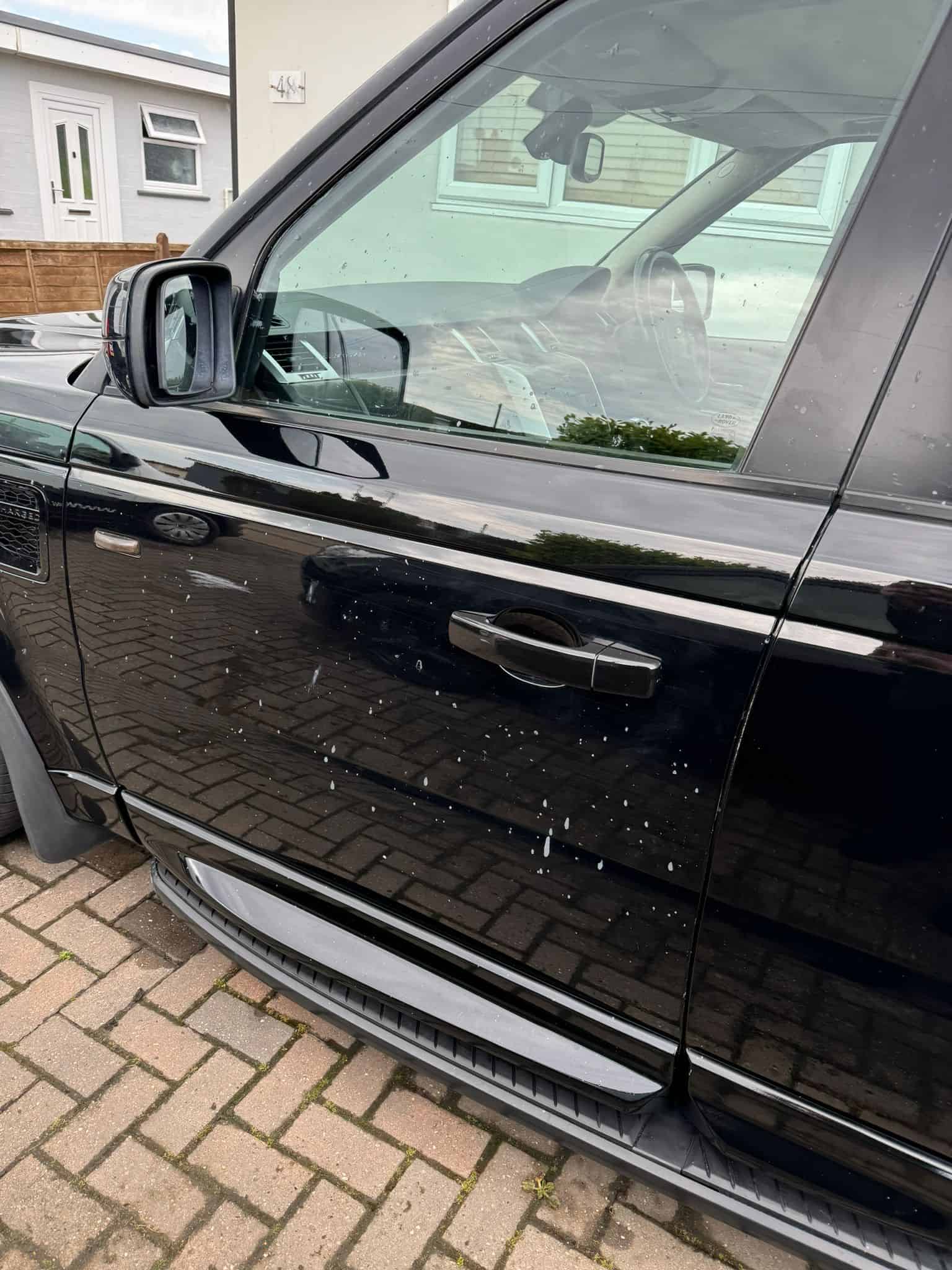 Car paint contamination removal in progress: test panels demonstrating successful liquid plastic removal from black vehicle paintwork by MAX WAX technicians